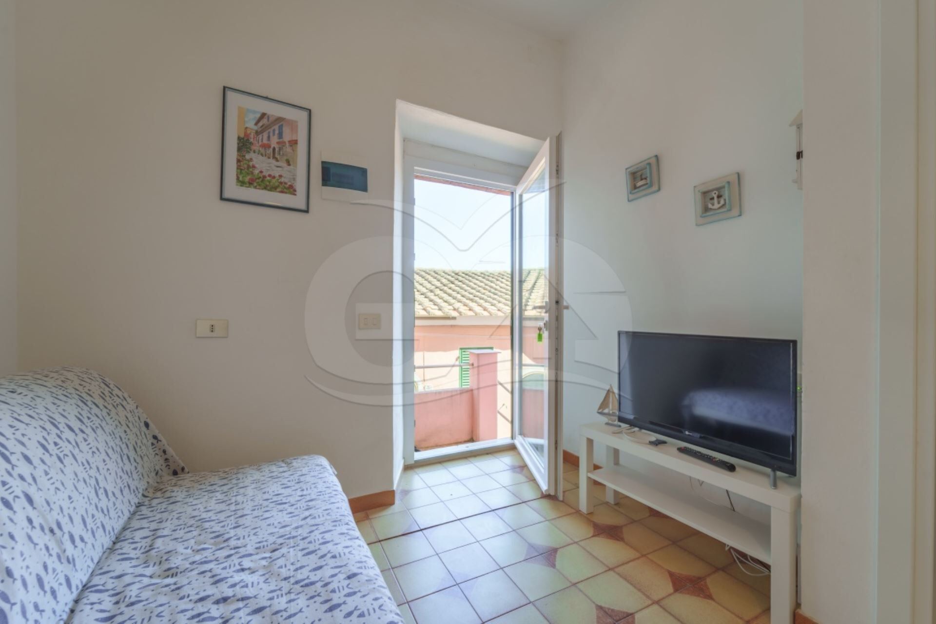 A room with a bed, a TV on a stand, and a door leading to an outdoor area.