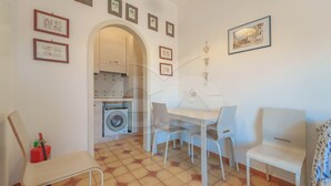 A small, clean room with a tiled floor, a washing machine, a table with chairs, and framed pictures on the walls. - NEL CUORE DI RIO MARINA (Rio Marina)