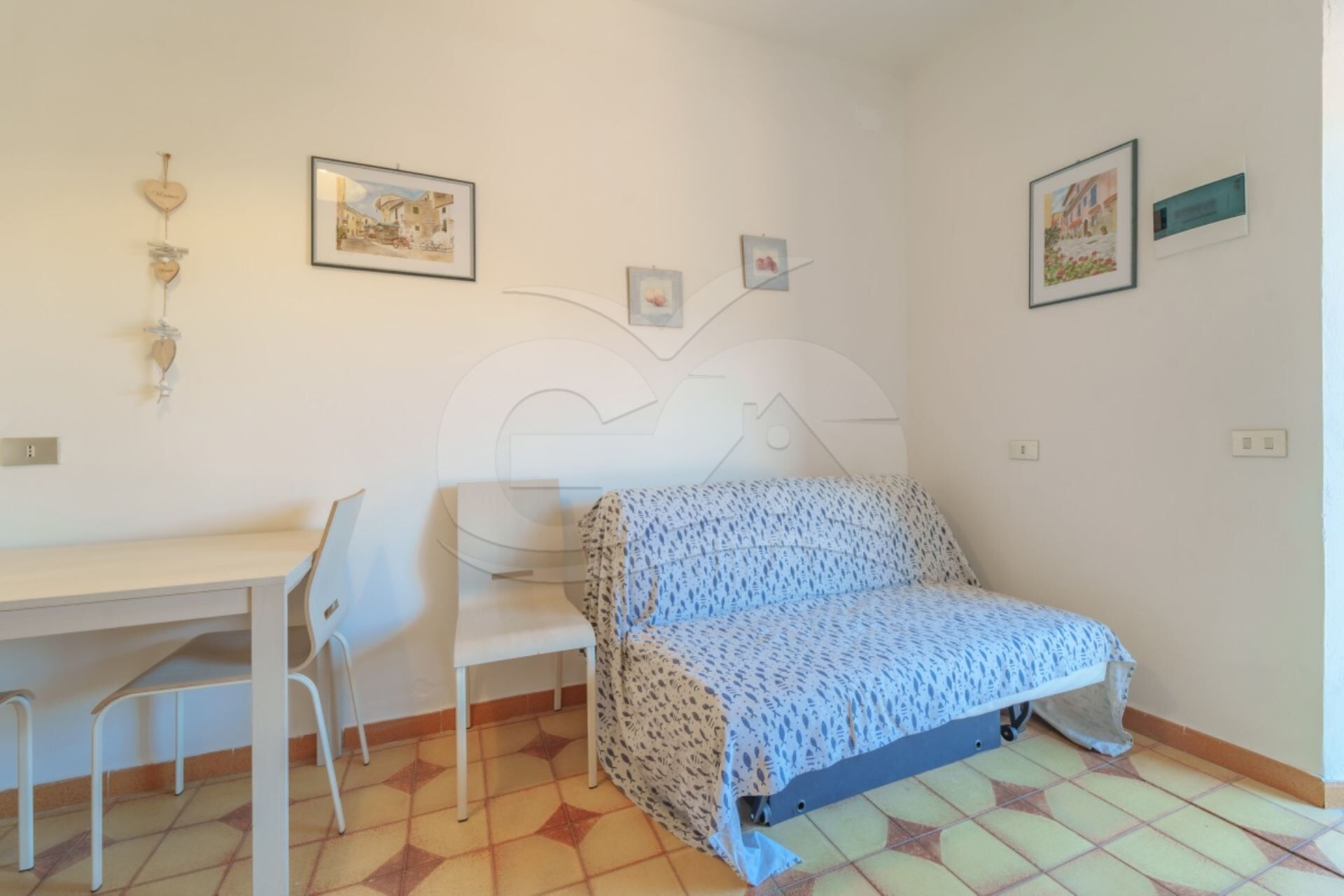 A small, clean room with a bed, a desk, and a chair. There are pictures on the wall.