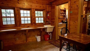 A wooden cabin interior with a sink, chair, table, and windows.