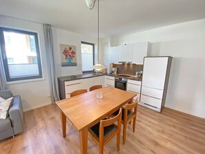 Une cuisine moderne avec des meubles blancs, une table à manger en bois et un canapé gris.