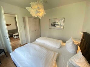 Une chambre avec deux lits, une armoire, une table de chevet, un luminaire suspendu et un tableau encadré au mur.