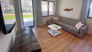 Een moderne woonkamer met een grijze bank, een witte salontafel en een houten kast met decoratieve gravures.
