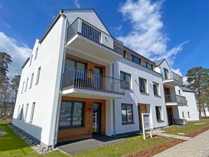 Un immeuble résidentiel moderne à plusieurs étages, doté de balcons, de grandes fenêtres et d’une pelouse bien entretenue.
