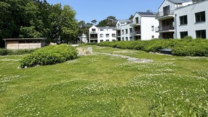 Een woonwijk met moderne, meer verdiepingen tellende gebouwen, een gazon met witte bloemen en dichte bomen op de achtergrond.