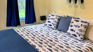 Una cama con cubrecama estampado con motivos de peces, una colcha azul y almohadas a rayas.
