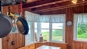 Interior de una cabaña de madera con una cama, ventanas y un colgador para ollas.