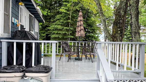 A wooden deck with a white railing, outdoor furniture, and a grill.