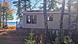 A single-story cabin with a front porch, a small deck, and a view of the ocean.