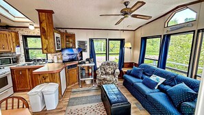 A compact RV interior with a kitchenette, a sofa, a chair, and a ceiling fan.