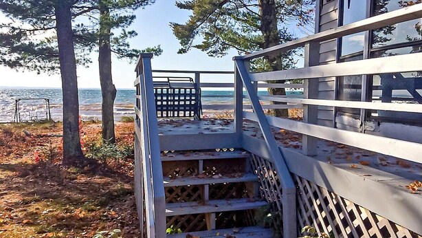 A wooden staircase leading to a deck with a railing, overlooking a beach and the sea.