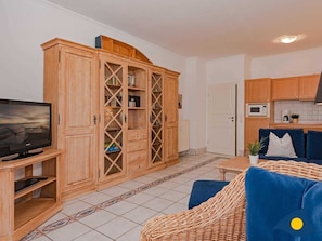 A living room with a television, a large wooden cabinet, a sofa, and a kitchen area with cabinets and a microwave. - Villa Vineta Whg. 11 - Vineta 11 (Heringsdorf)