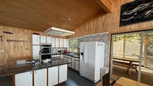 A modern kitchen with wooden cabinetry, a central island, and a large window providing a view of the outdoors. - Feeling Superior - Cliffside Home with Amazing Lake Views (La Pointe)