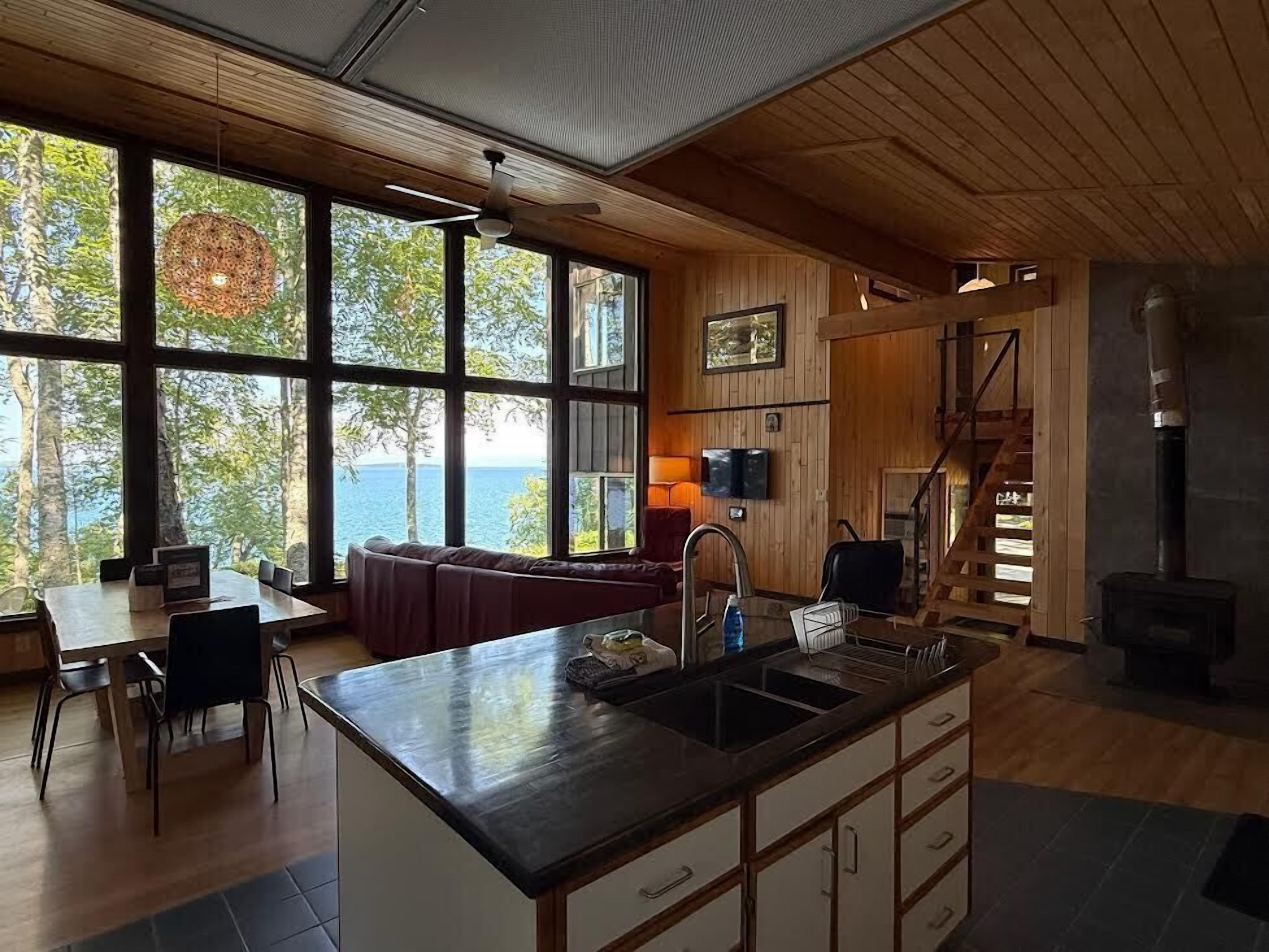 A modern kitchen with a large island, wooden walls, and a view of the outdoors.