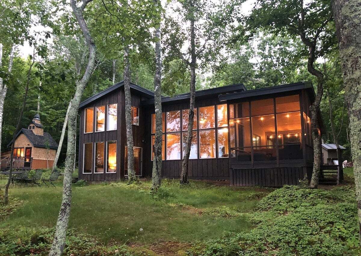 Une cabane dotée de grandes fenêtres, d’une terrasse et d’une petite dépendance attenante.