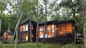 A cabin with large windows, a deck, and a small attached structure. - Feeling Superior - Cliffside Home with Amazing Lake Views (La Pointe)