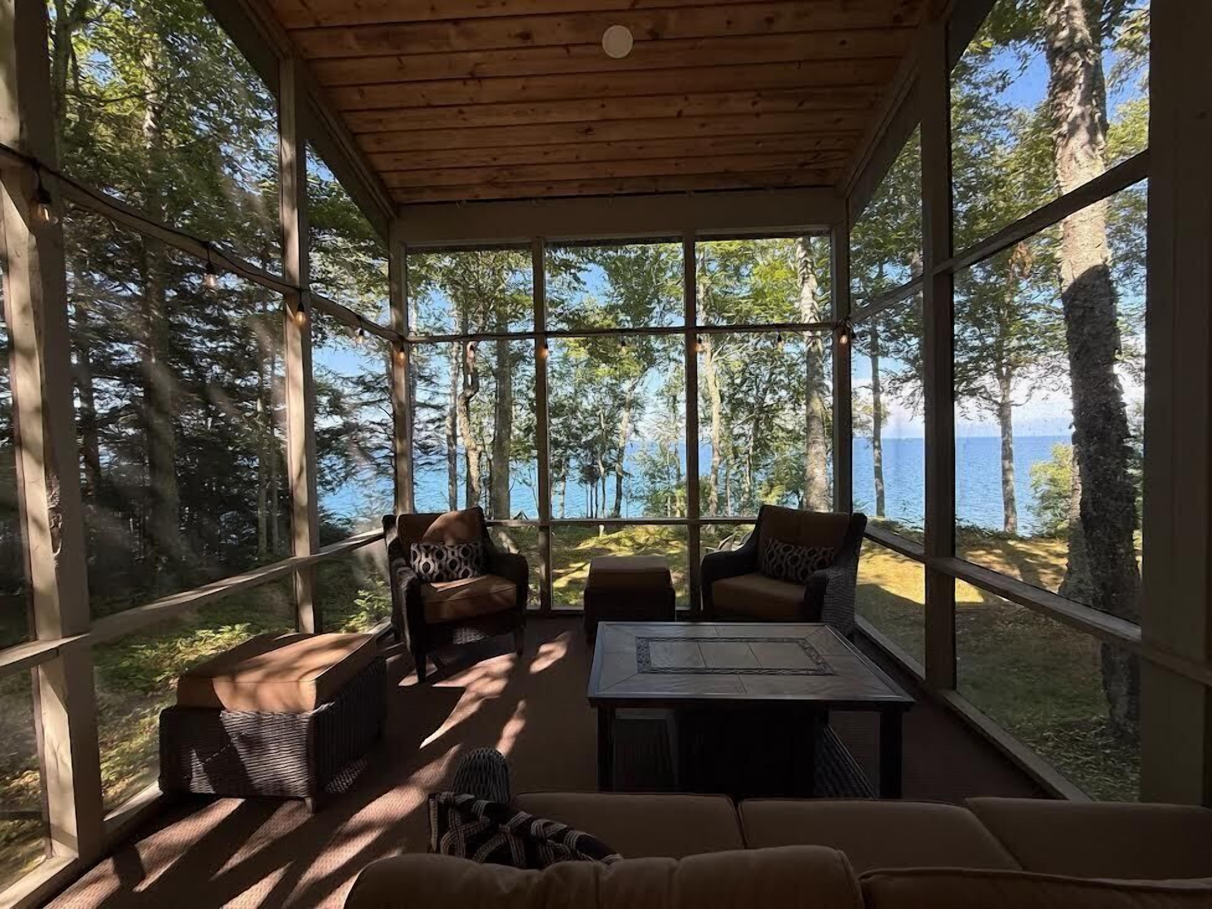 Un espacio de estar al aire libre cubierto con muebles de mimbre y vistas al bosque y al agua.