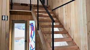 A wooden staircase with a black metal handrail, leading to an upper level. - Feeling Superior - Cliffside Home with Amazing Lake Views (La Pointe)
