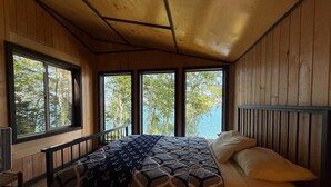 A bedroom with a bed, windows, and a view of trees and water. - Feeling Superior - Cliffside Home with Amazing Lake Views (La Pointe)
