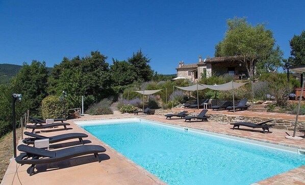 A pool area with lounge chairs, a stone building in the background, and a clear blue sky.