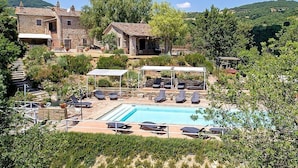 A stone building with a pool, surrounded by greenery and hills.