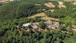 An aerial view of a rural property with a stone house surrounded by dense forest, a swimming pool, and terraced fields. - Villa Cenobio D: A characteristic and welcoming apartment that is part of an ancient country house made of stone, with Free WI-FI. (Umbertide)
