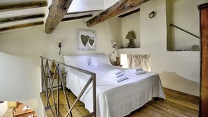 A bedroom with a wooden ceiling, a bed with white linens, a nightstand with a lamp, and a wall-mounted clock. - Villa Cenobio D: A characteristic and welcoming apartment that is part of an ancient country house made of stone, with Free WI-FI. (Umbertide)