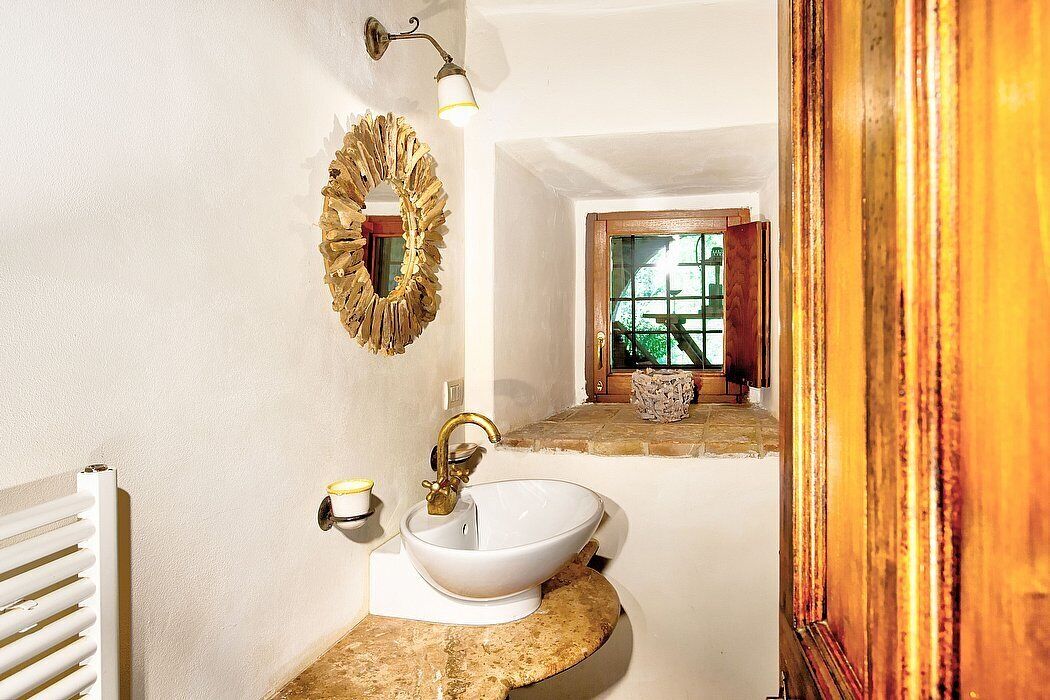 A bathroom with a white sink, gold faucet, and a decorative wreath on the wall.
