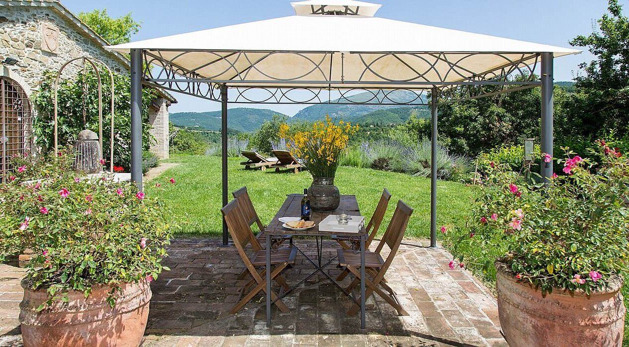 Una terrazza esterna con tavolo e sedie, circondata da piante in vaso e un edificio in pietra.