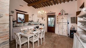 A rustic kitchen with a dining table, chairs, a chandelier, and a white cabinet.