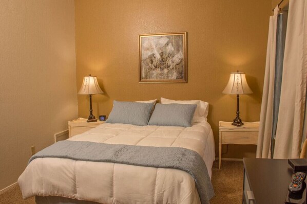 Een hotelkamer met een bed, twee nachtkastjes, een lamp op elk nachtkastje, een schilderij aan de muur en een gordijn voor het raam.