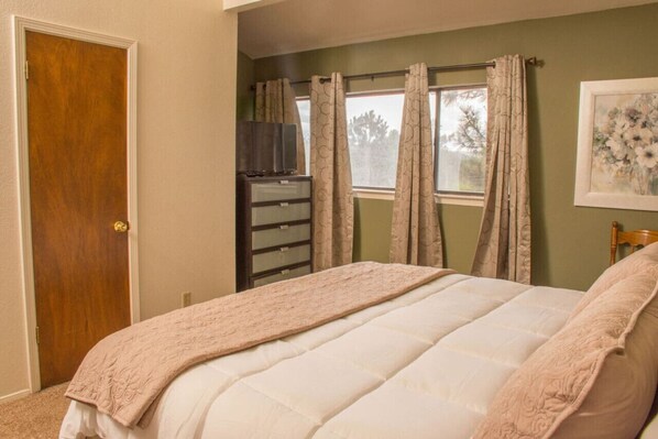 Un dormitorio con cama, cómoda, televisor y ventana con cortinas.