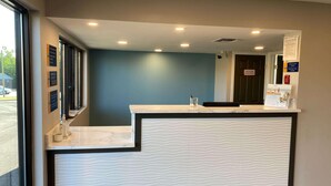 A reception desk with a marble top and a textured white panel. There are signs on the wall and a door with a fire safety sign. - Homelodge Newnan (Newnan)