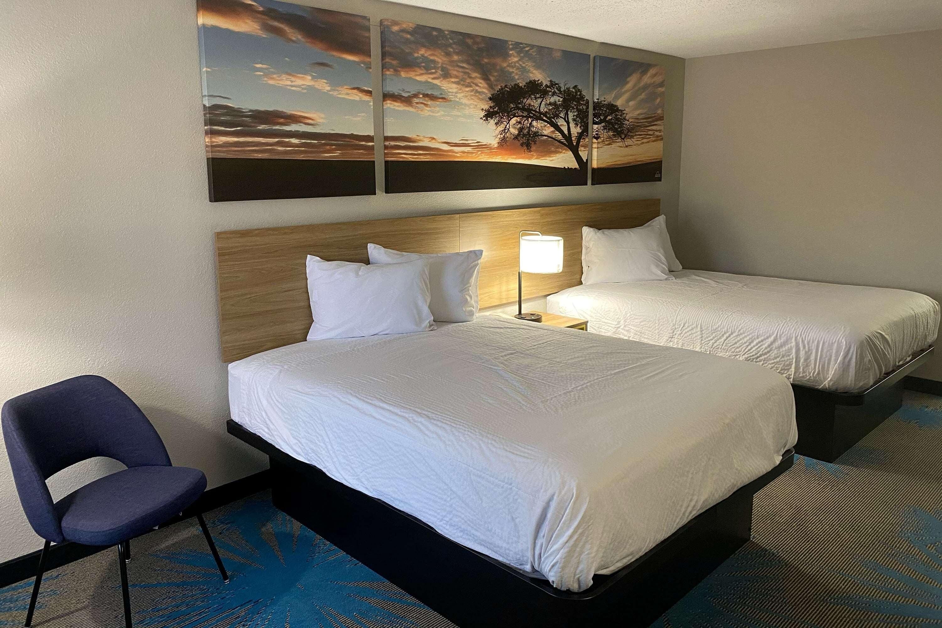 A hotel room with two beds, a chair, and a wall with three paintings.