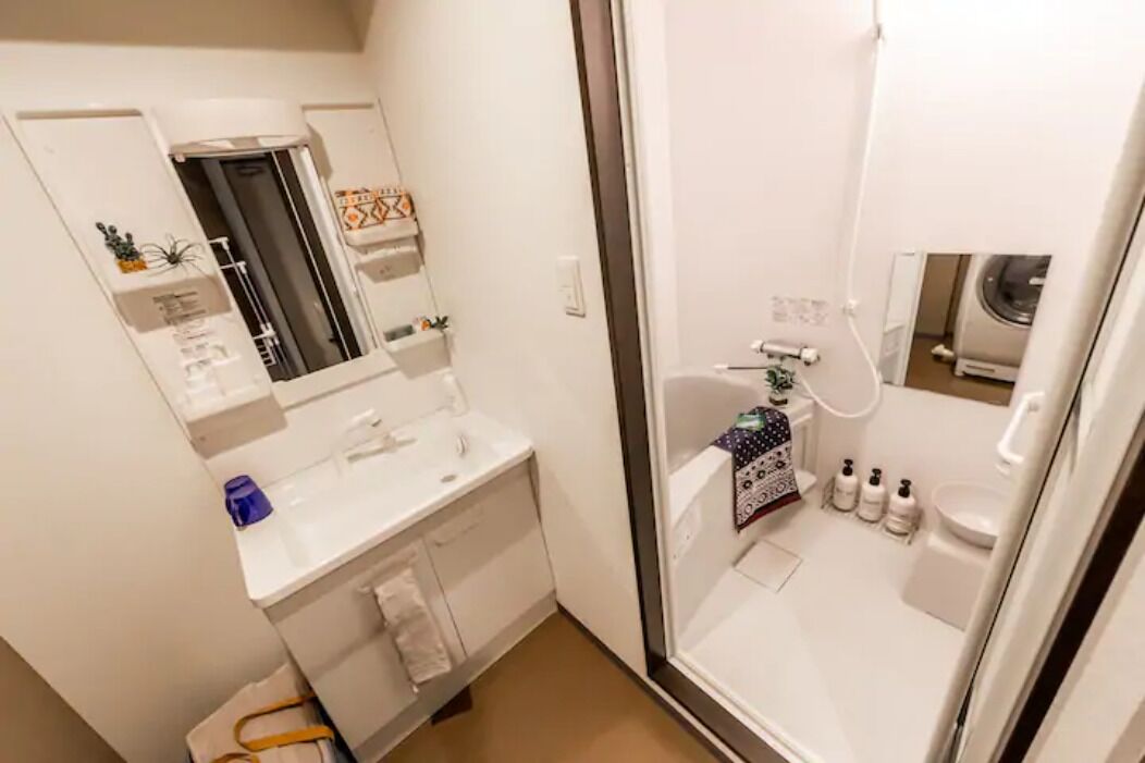 Une petite salle de bain avec un lavabo blanc, un miroir et des toilettes. On y trouve une petite étagère avec des articles de toilette et un porte-serviettes.
