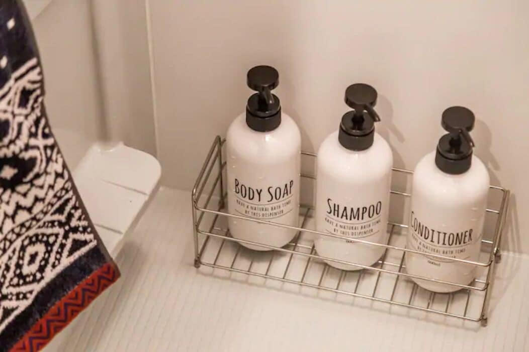 Un estante de baño con tres botellas de jabón corporal, champú y acondicionador.