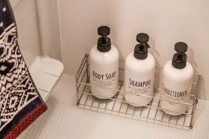 A bathroom shelf with three bottles of body soap, shampoo, and conditioner.