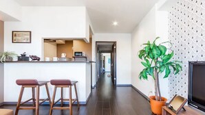 Een moderne woonkamer met een keukenhoek, een eettafel, een grote potplant en een flatscreen televisie.