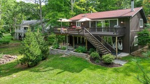 A two-story house with a deck, outdoor seating, and a staircase leading to the upper level. - Discover The Sandy Moose: a spacious 4-bedroom retreat in serene Fennville, MI. (Fennville)