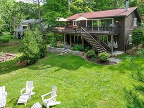 A two-story house with a deck, outdoor seating, and a staircase leading to the upper level. - Discover The Sandy Moose: a spacious 4-bedroom retreat in serene Fennville, MI. (Fennville)