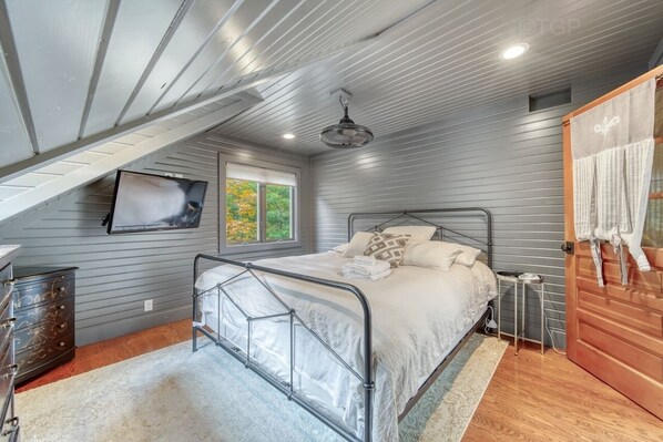 A bedroom with a metal bed frame, a wooden door, and a window with a view of trees.