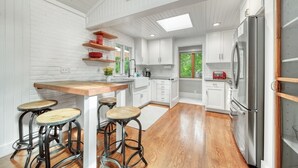 A modern kitchen with white cabinetry, a wooden island with stools, and a stainless steel refrigerator. - Discover The Sandy Moose: a spacious 4-bedroom retreat in serene Fennville, MI. (Fennville)