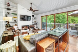 A spacious living room with a large window, a ceiling fan, and a wooden deck visible through the glass doors.