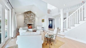A modern living room with a stone fireplace, white furniture, and a glass coffee table.