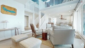 A spacious living area with a high ceiling, a staircase, and a dining area.