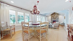 A dining area with a round glass table, wooden chairs, a chandelier, and a stone fireplace.