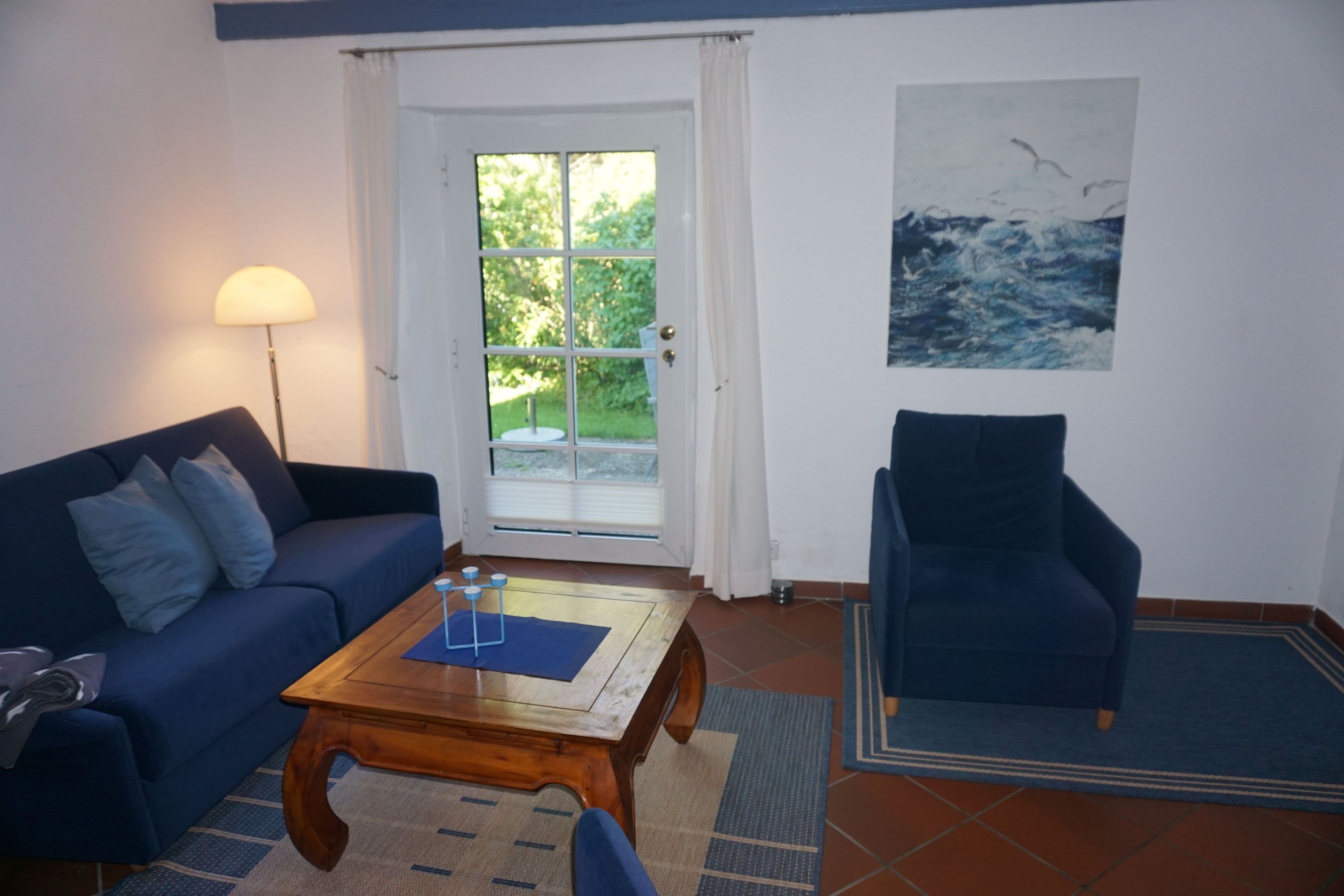 A living room with a sofa, armchair, coffee table, and a painting on the wall.