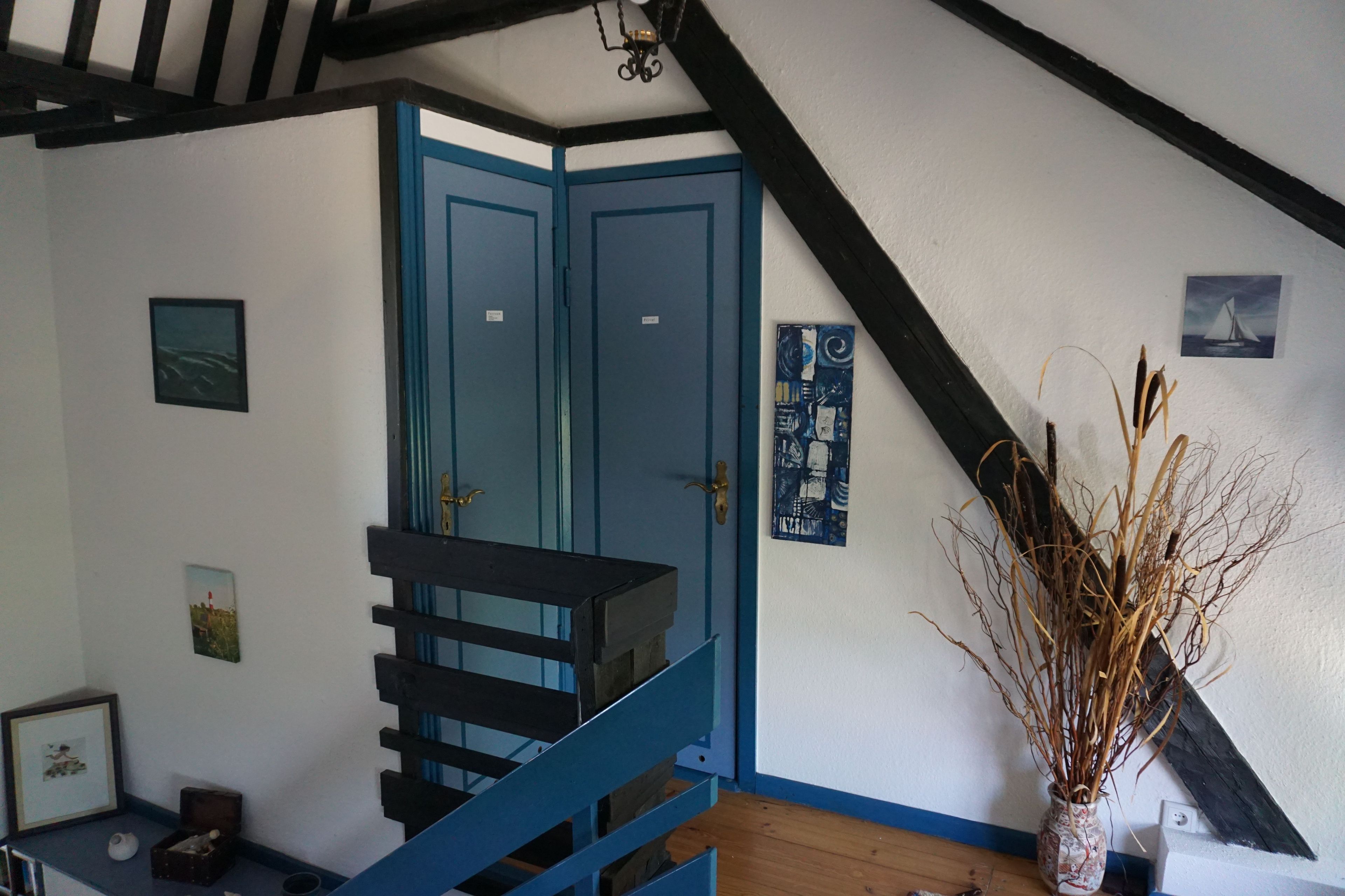 A room with a blue staircase, a vase with dried plants, and a sailboat picture on the wall.