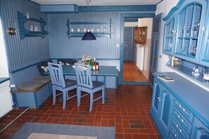 A kitchen with blue cabinetry, a dining table with chairs, and a hanging light fixture. - FW Geltinger Birk - Luckow Georg Asmussen Haus (Pommerby)