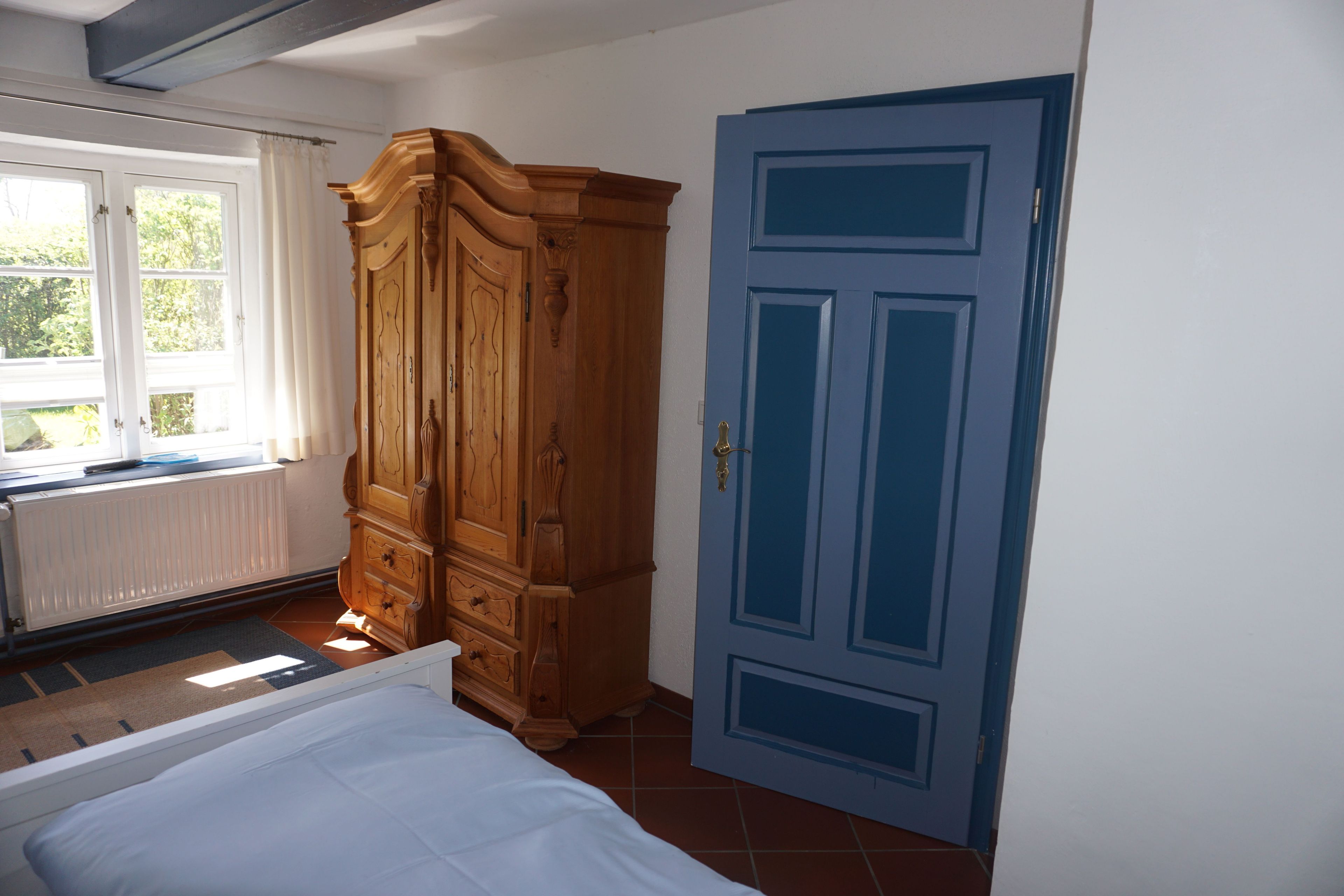 A bedroom with a bed, a wooden wardrobe, a blue door, and a window with curtains.